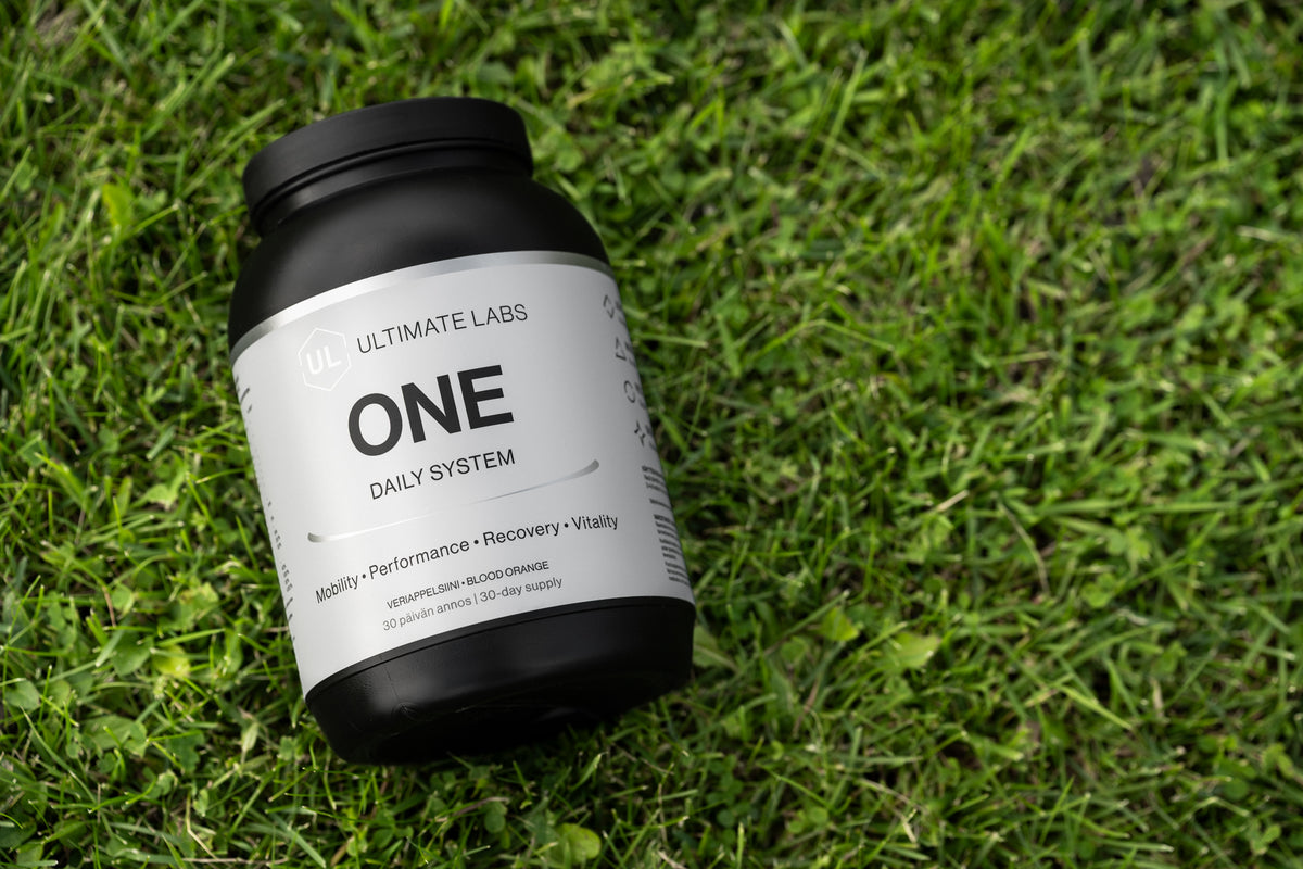 Ultimate Labs ONE Daily System -ravintolisäpurkki lepää vihreällä nurmikolla
