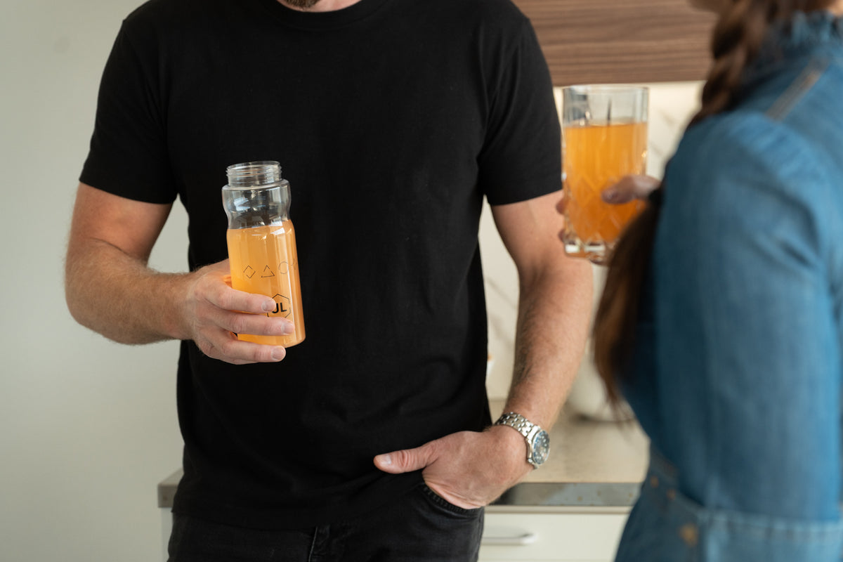 Ultimate Labs ONE Daily System -ravintolisäjauheesta sekoitettu, veriappelsiinin makuinen juoma ja kaksi henkilöä pitelemässä valmiita juomia